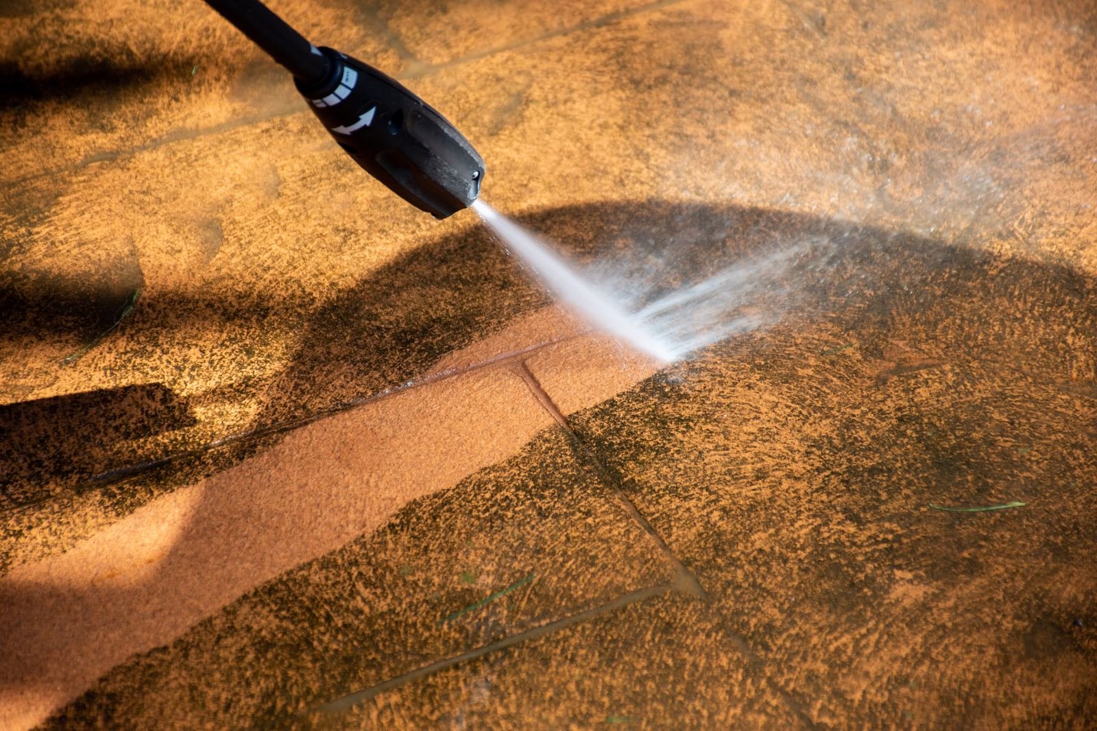 Patio tile surface half cleaned by pressure washing showing before and after contrast