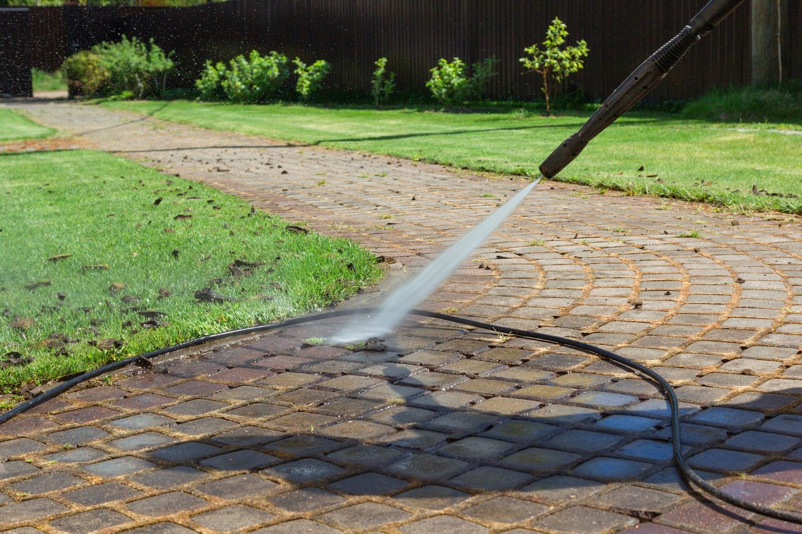 Pressure washing wand cleaning paver walkway with visible clean and dirty contrast