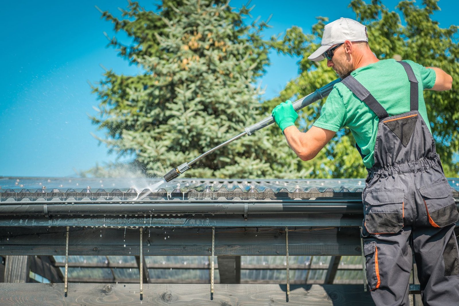 Technician soft washing an asphalt shingle roof at a Greenville, SC home on a sunny day
